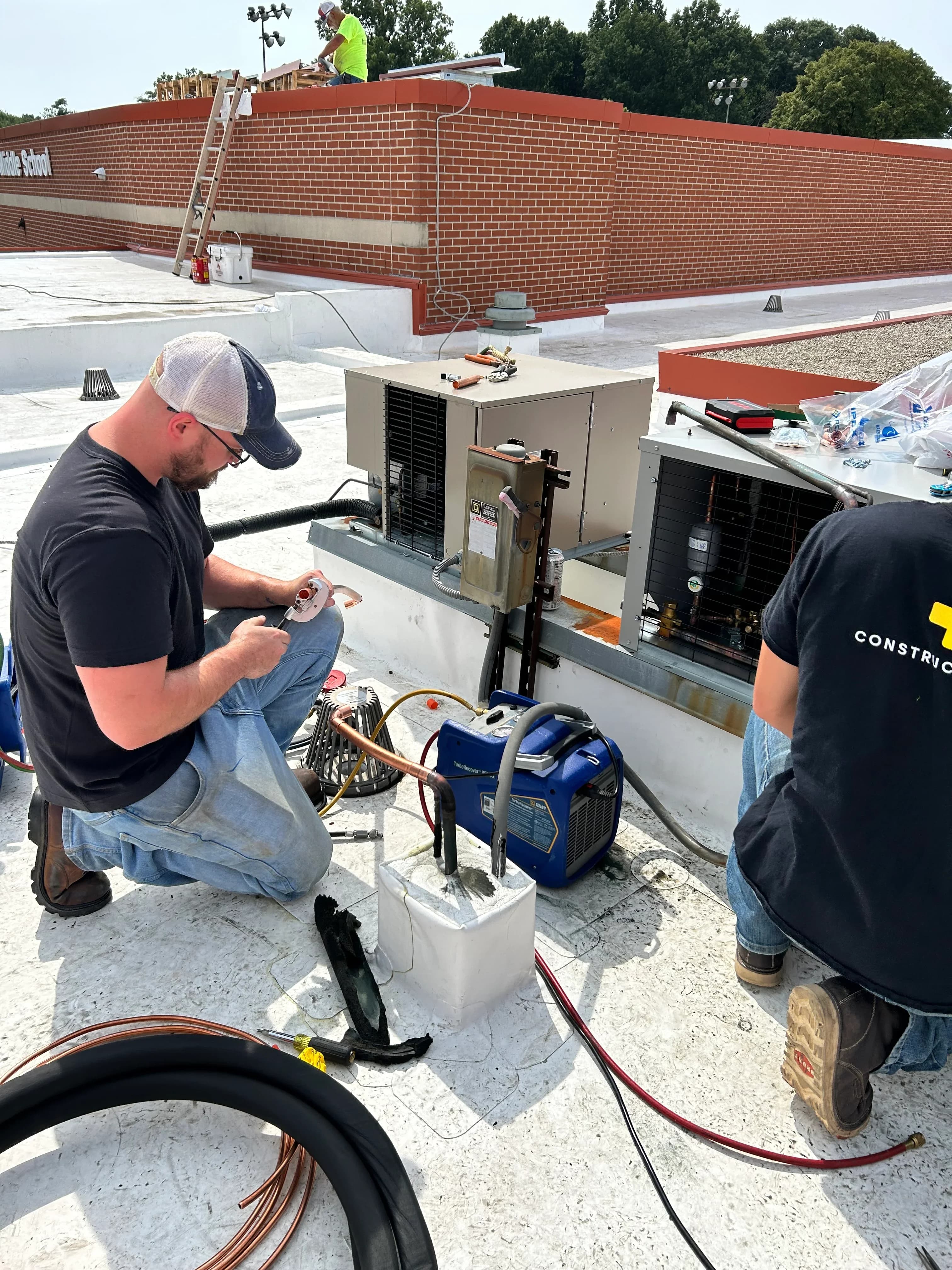 Two technicians repairing a rooftop condensing unit with gauges and torch