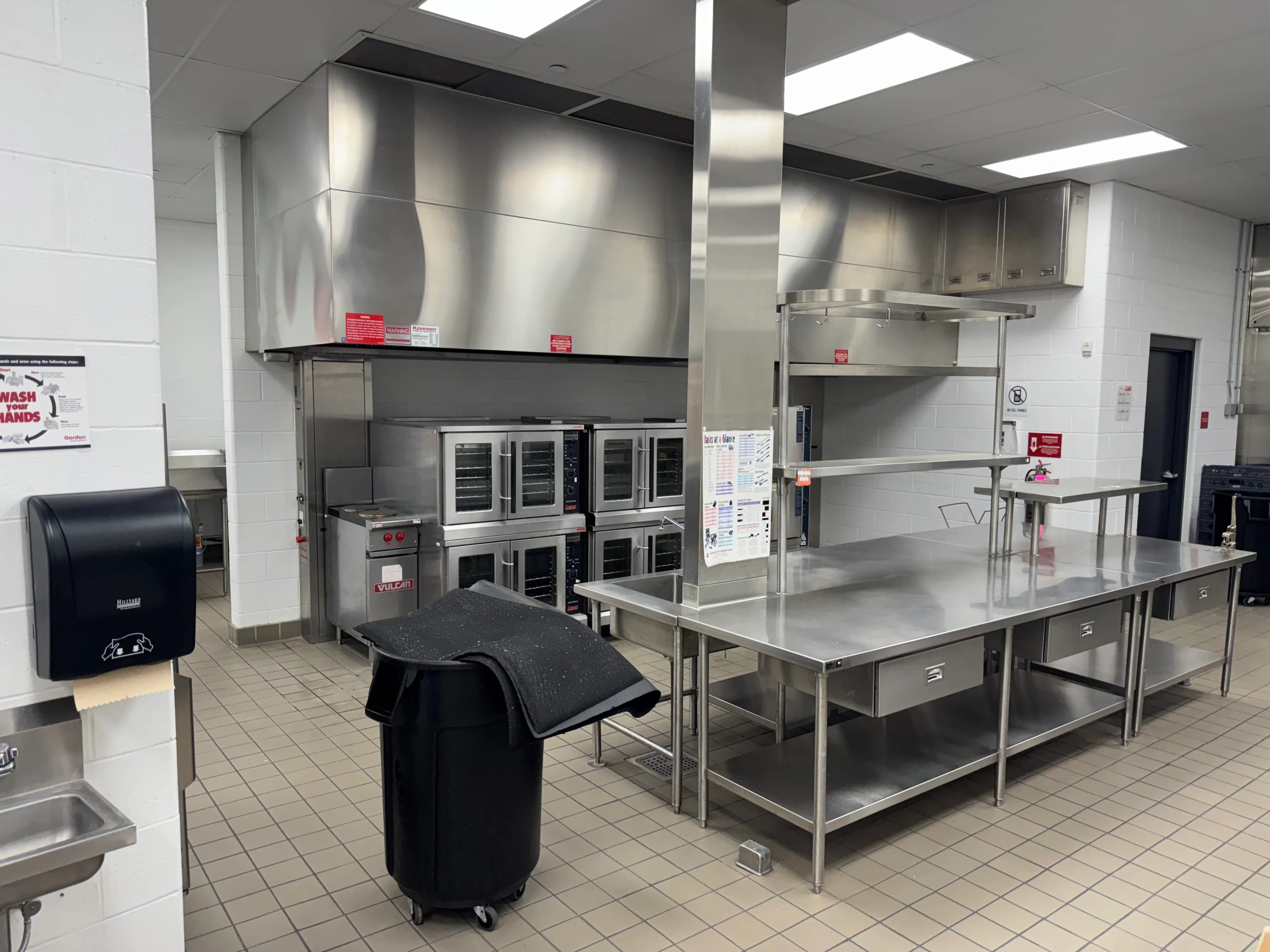 A stainless commercial kitchen cook line with convection ovens and an exhaust hood