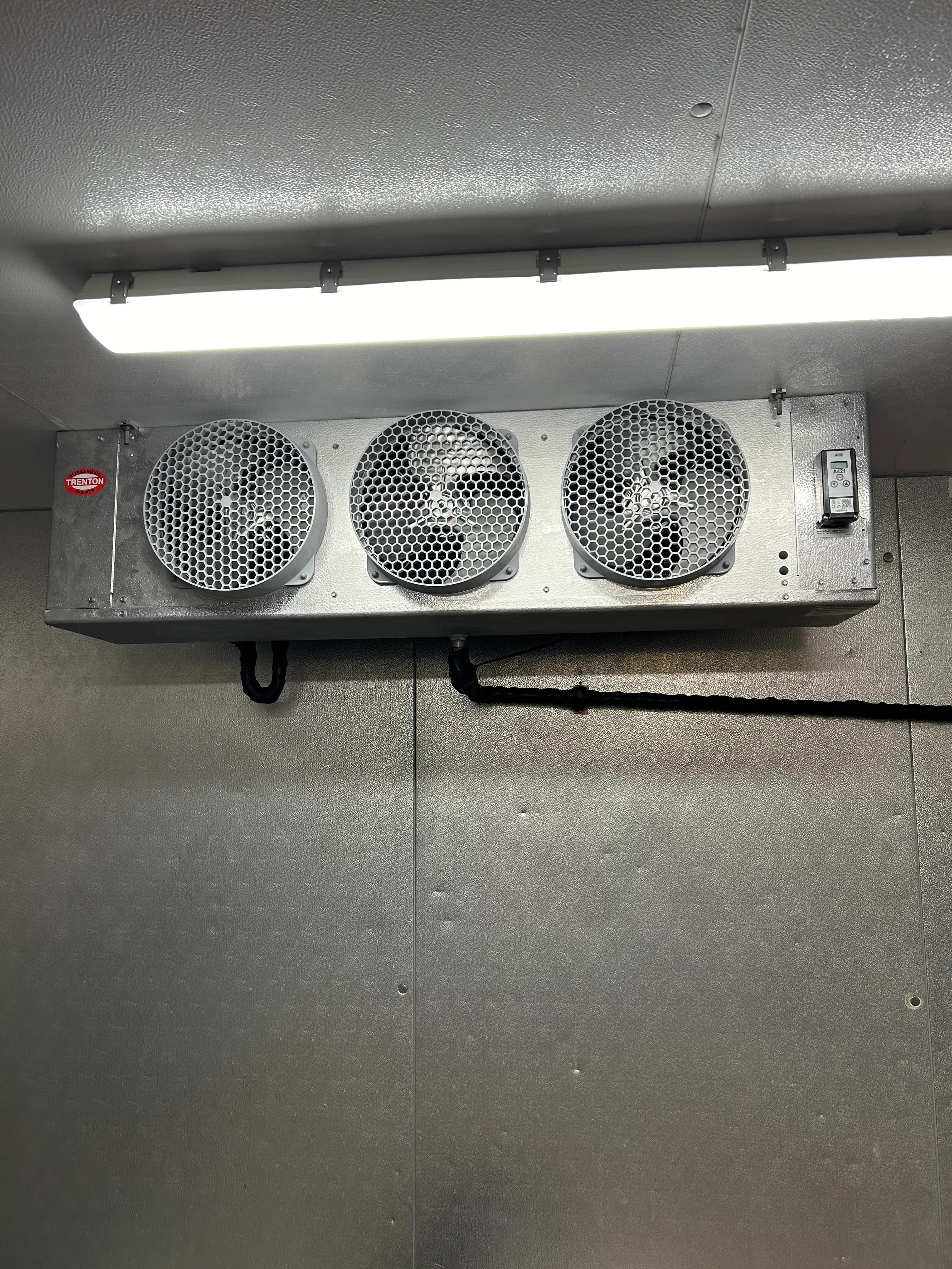 A three-fan evaporator coil mounted inside a commercial walk-in cooler